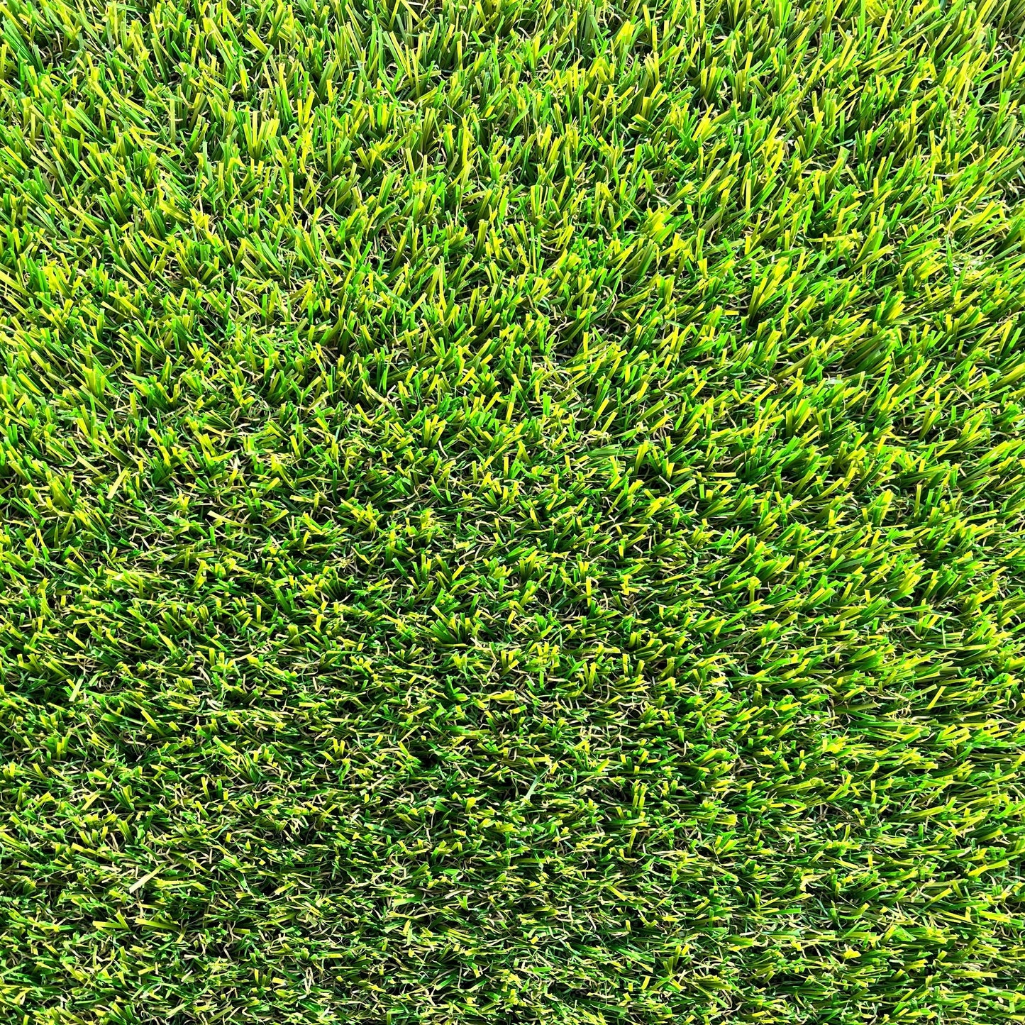 Une vue macro de brins de gazon synthétique, montrant les détails des fibres plastiques et leur base tissée noire, avec des nuances de vert et des touches de brun.