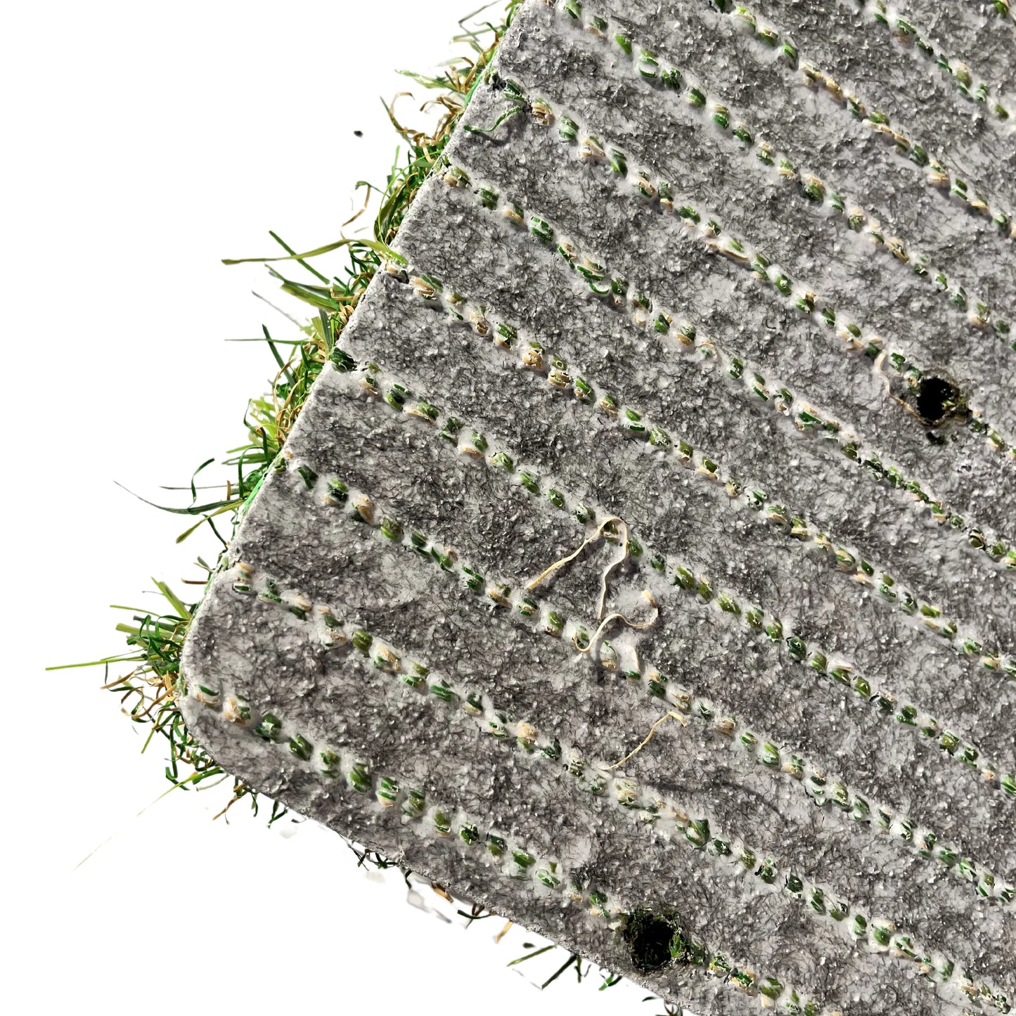 Gros plan de l’envers d’un rouleau de gazon synthétique avec des lignes de couture vertes et une texture en relief, montrant les fibres du gazon sortant légèrement de la base.