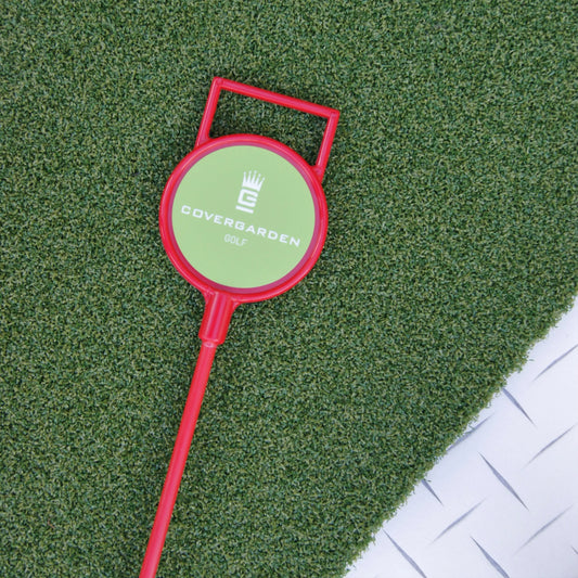 Marqueur de golf rouge avec poignée, portant le logo 'COVERGARDEN GOLF', posé sur une surface de gazon synthétique vert.