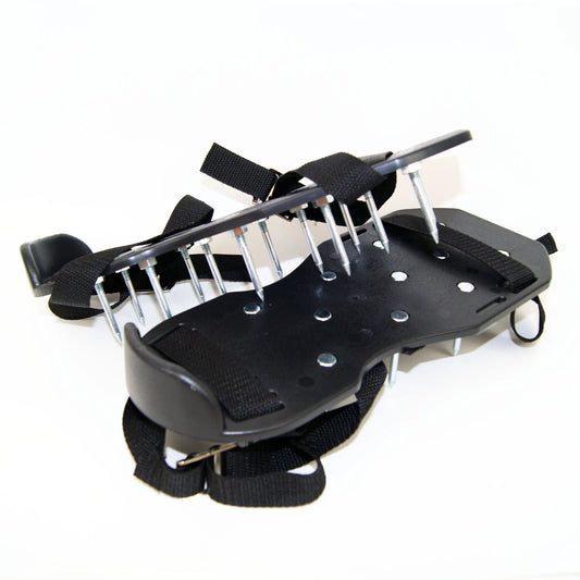 Une paire de patins aérateur de pelouse noire avec des semelles rigides et des pointes métalliques robustes fixées par des écrous. Les patins possèdent des sangles noires ajustables pour les attacher aux chaussures, facilitant l'aération de la pelouse.