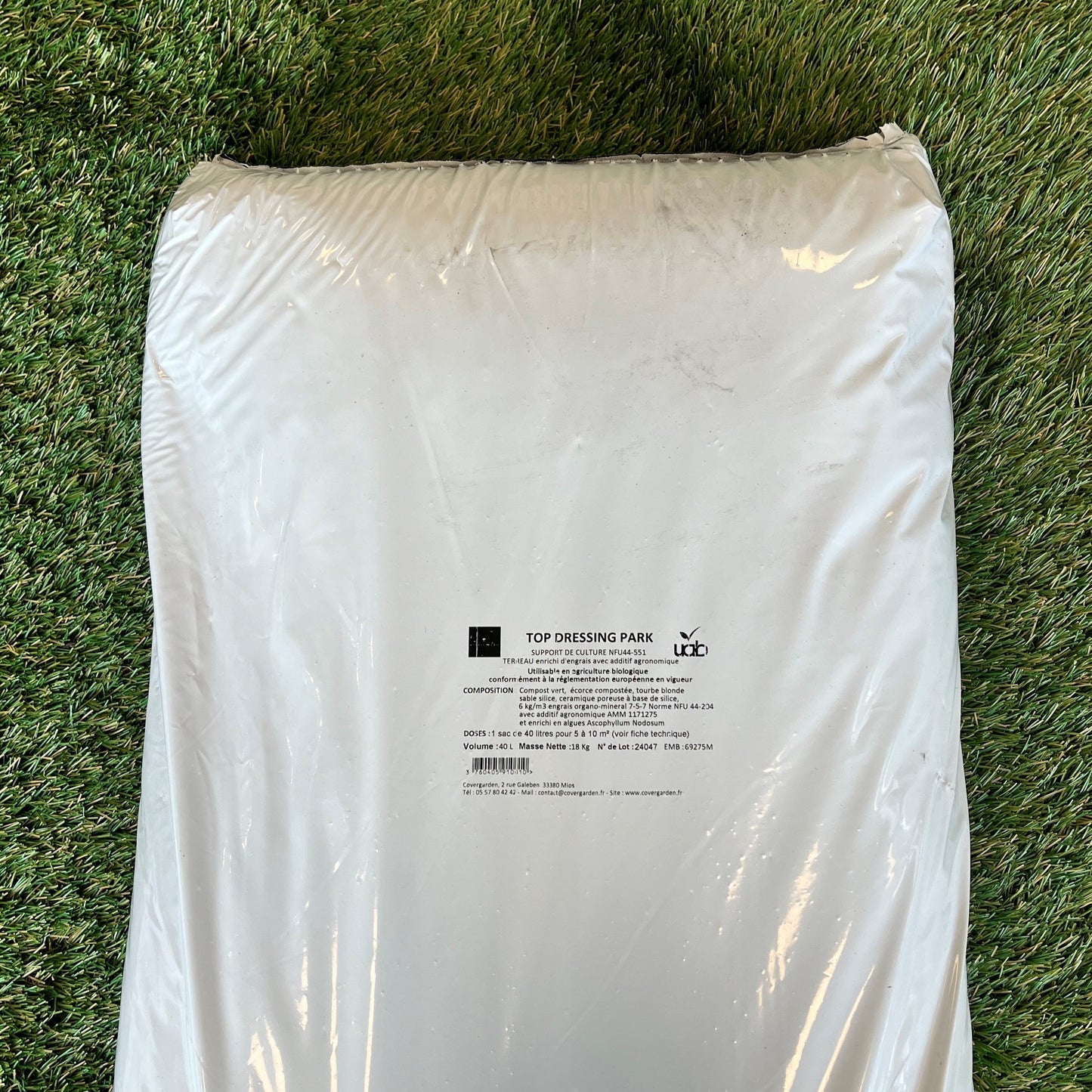 Un sac blanc de produit "Top Dressing Park" posé sur une pelouse. L'étiquette imprimée au centre indique la composition : compost vert, écorce compostée, tourbe blonde, céramique poreuse et sable, avec un enrichissement en algues et engrais organominéral.