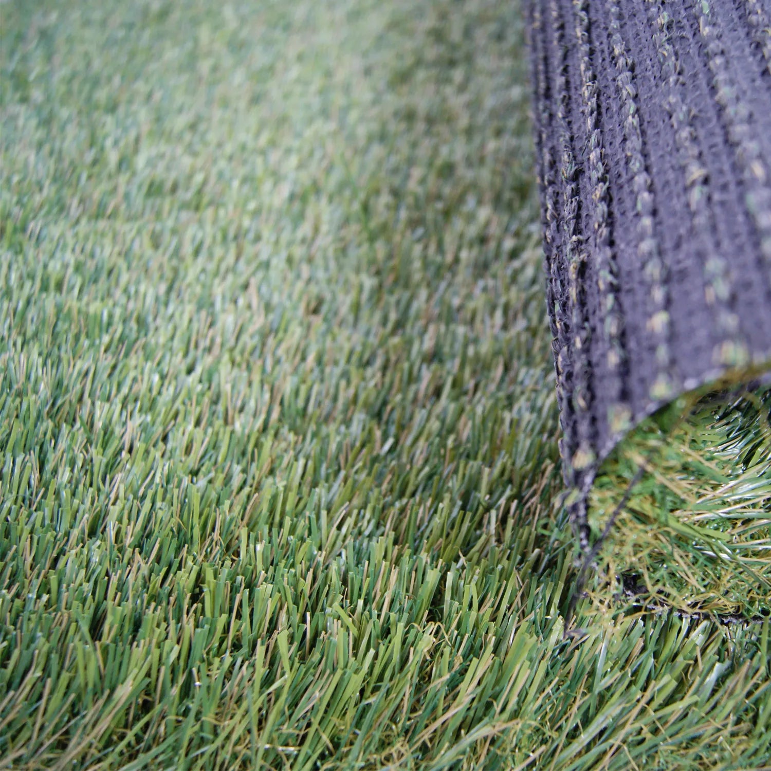 Gazon synthétique vert avec des fibres réalistes, et un morceau enroulé montrant le dessous du tapis noir texturé.