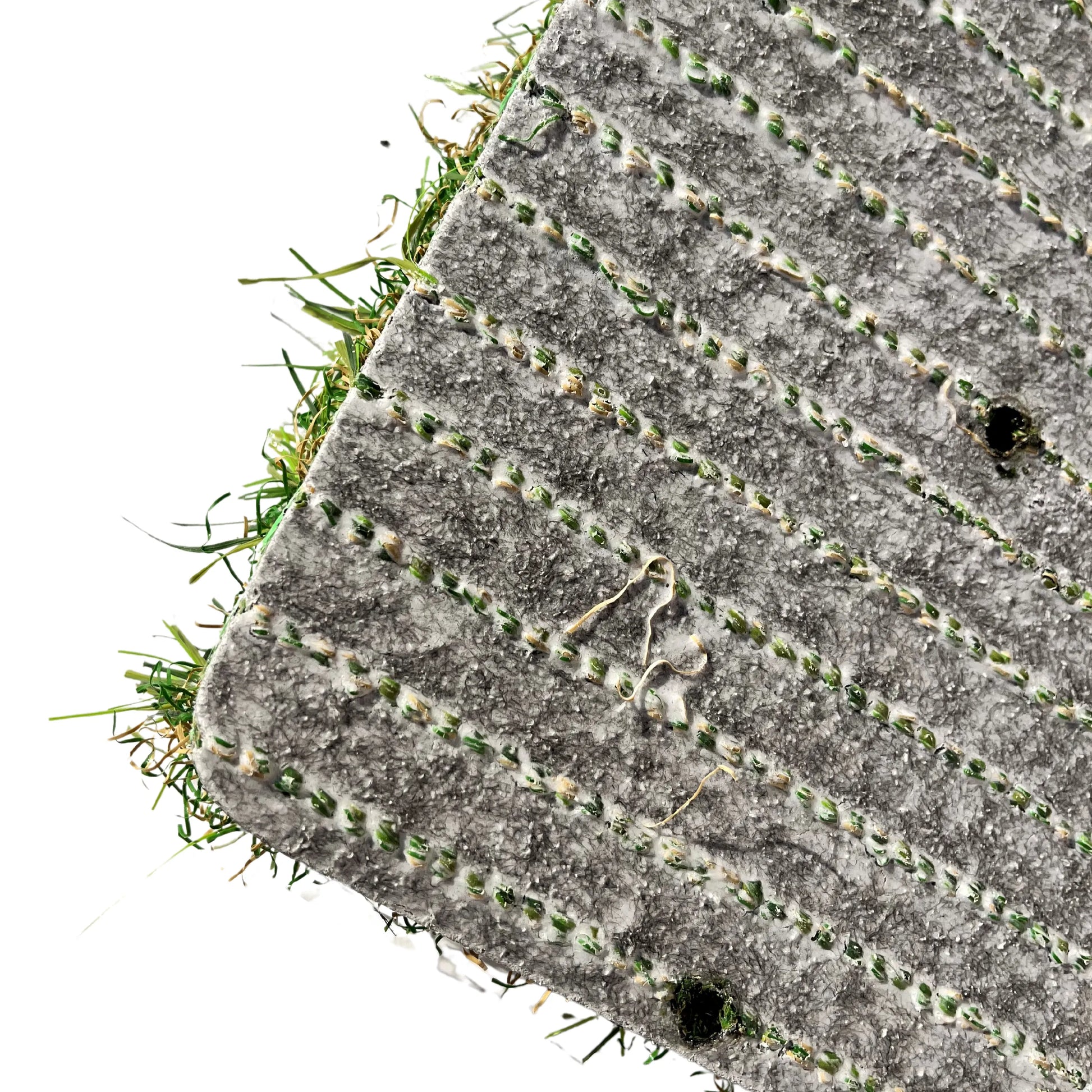 Gros plan de l’envers d’un rouleau de gazon synthétique avec des lignes de couture vertes et une texture en relief, montrant les fibres du gazon sortant légèrement de la base.