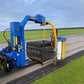 Machine agricole bleue de type récolteuse avec des rouleaux de gazon fraîchement enroulés. La machine est posée sur un champ, avec des rangées de gazon bien entretenues à l'arrière-plan.