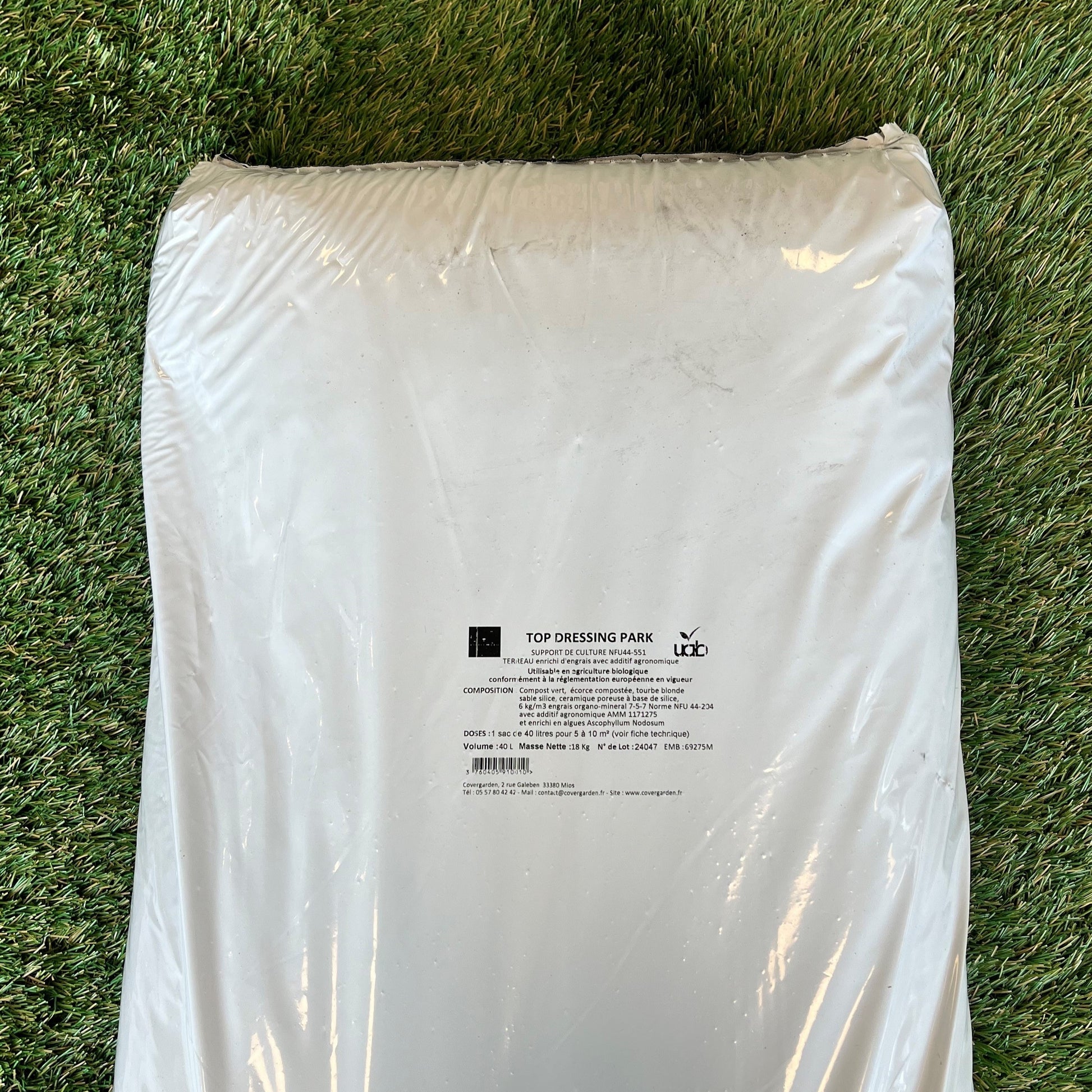 Un sac blanc de produit "Top Dressing Park" posé sur une pelouse. L'étiquette imprimée au centre indique la composition : compost vert, écorce compostée, tourbe blonde, céramique poreuse et sable, avec un enrichissement en algues et engrais organominéral.