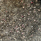 Gros plan d'un substrat de terre composé de petits morceaux d'écorce, de terre noire, de sable et de granulés colorés, principalement roses et jaunes, représentant un mélange enrichi pour gazon.